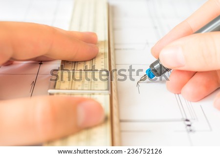 Hand holds the pen and a slide rule to create a drawing. Angle view