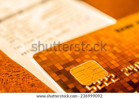 Credit card and check from shopping on the table, focus on the microchip of the card. In yellow tone