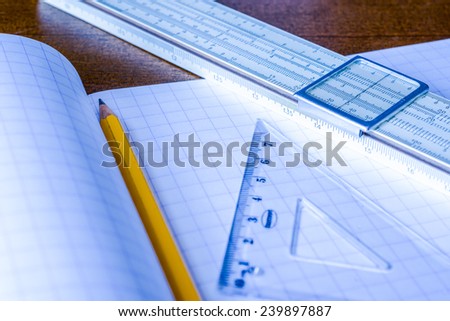 Schemes the pencil and triangle with slide rule on the table in the school. In blue tone
