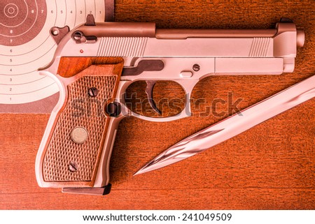 Target shooting, the gun and the target with the knife on the table. Top view, in red tone