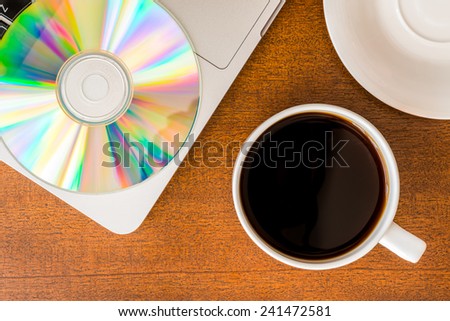Work in the office, coffee cup and a plate with an optical disk with laptop on the wooden table