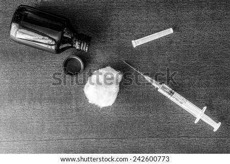 Cure the disease, a solution, and a syringe for injection with wadding on the table. Top view, in black and white tone