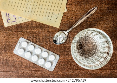 Cure the disease, tablets in the spoon with a glass of water and prescriptions from the doctor on the table. Top view, in the old colors
