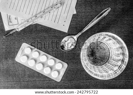 Cure the disease, tablets in the spoon with a glass of water and prescriptions from the doctor on the table. Top view, in the black and white colors