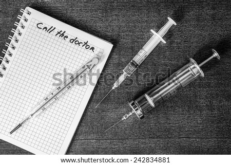 Call the doctor, a two syringe and thermometer on the table. Top view, in the black and white tones
