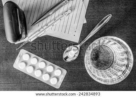 Cure the disease, tablets in the spoon with a glass of water and prescriptions from the doctor and stamp on the table. Top view, in the black and white tones