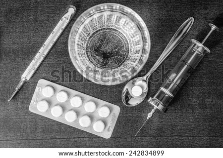 Cure the disease, an injection syringe and take the pills in the spoon. Top view, in the black and white tones