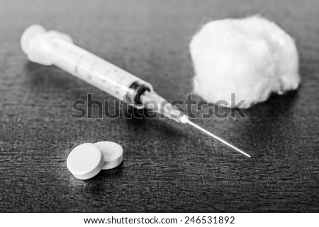 Syringe injection with a wadding and a tablets on the table. Angle view, in black and white tones