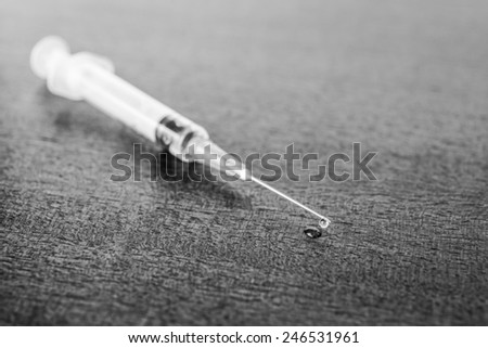 Medicine flows from the syringe and spread out on the table. Angle view, in black and white tones