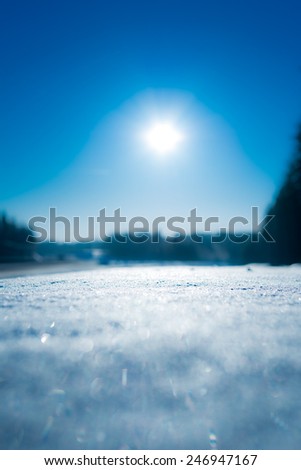 View of the snow-covered road with curb, the sun rises from the horizon. In blue tones
