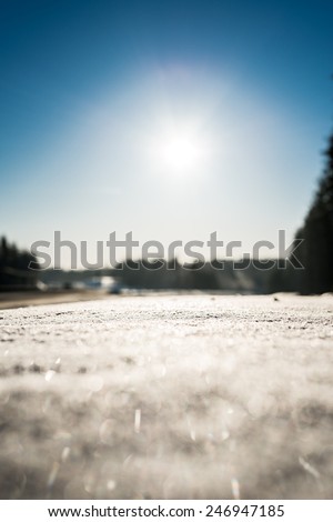 View of the snow-covered road with curb, the sun rises from the horizon