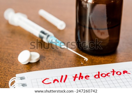 Call the doctor, medicine flows from the syringe and spread out on the table, standing next to the beaker with medicine. Angle view, focus on the sign