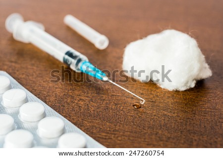 Medicine flows from the syringe and spread out on the table, lies next to a cotton swab and a pills. Angle view