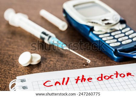Call the doctor, medicine flows from the syringe and spread out on the table, lies next to the phone. Angle view, focus on the sign, in old tones