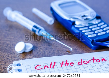 Call the doctor, medicine flows from the syringe and spread out on the table, lies next to the phone. Angle view, focus on the sign, in blue tones