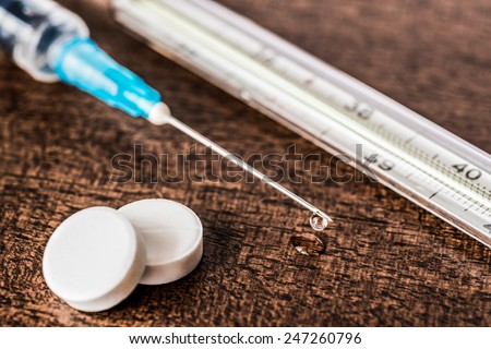 Medicine flows from the syringe and spread out on the table, lie next to pills and thermometer. Angle close up view, in old tones