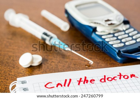 Call the doctor, medicine flows from the syringe and spread out on the table, lies next to the phone. Angle view, focus on the sign