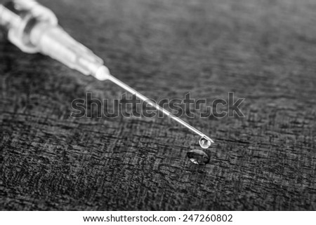 Medicine flows from the syringe and spread out on the table. Angle close up view, in black and white tones