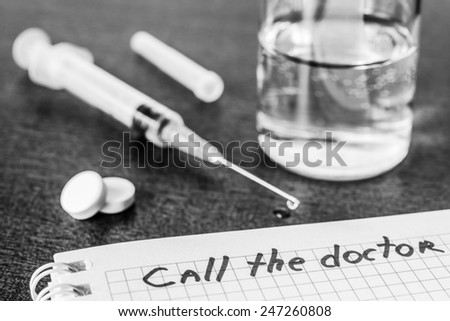 Call the doctor, medicine flows from the syringe and spread out on the table. Angle view, focus on the sign, in black and white tones