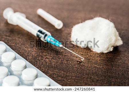 Medicine flows from the syringe and spread out on the table, lies next to a cotton swab and a pills. Angle view, in old tones