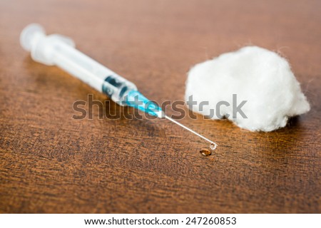 Medicine flows from the syringe and spread out on the table, lies next to a cotton swab. Angle view