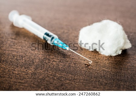 Medicine flows from the syringe and spread out on the table, lies next to a cotton swab. Angle view, in old tones
