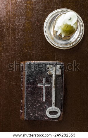 Key and Bible on the wooden desk with a candle. In brown tones