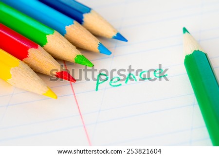 Word peace written in a notebook with colored pencils, green pencil lying on the notebook