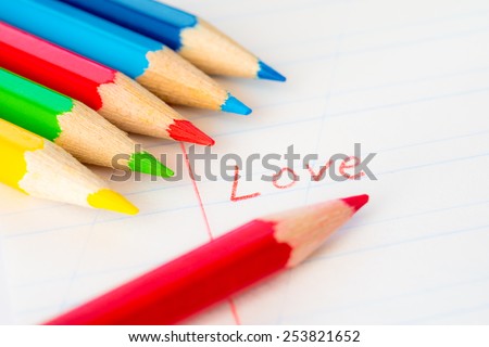 Word love written in a notebook with colored pencils, red pencil lying on the notebook