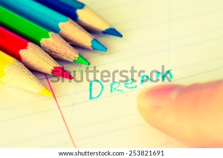 Word dream written in a notebook with colored pencils, finger points to the dream. Image in warm toning