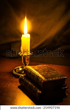 Bible and old books and candle on a wooden table. Focus on the old books, image vignetting and in yellow toning