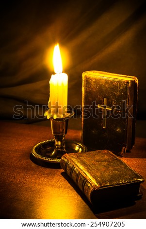 Bible and old book and candle on a wooden table. Focus on the old book, image vignetting and in yellow toning