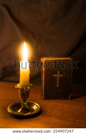 Old bible and candle on a wooden table. Focus on the bible