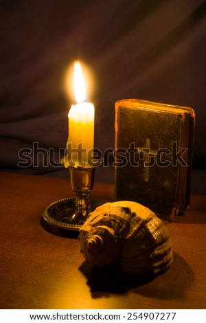 Old bible and candle with sea shell on a wooden table. Focus on the sea shell