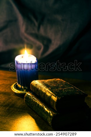 Bible and old books and candle on a wooden table. Focus on the old books, image in yellow-blue toning