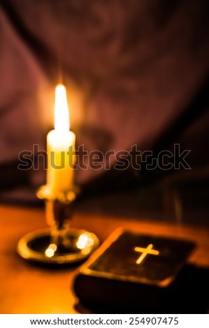 Old bible and candle on a wooden table. Image is out of focus, with lightning cross on the bible