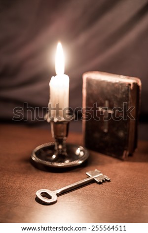 Old bible and candle with key on a wooden table. Focus on the key, image in old tones