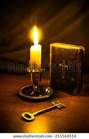 Old bible and candle with key on a wooden table. Focus on the key, image vignetting and in yellow toning