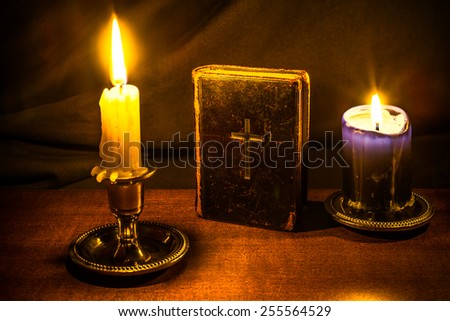 Bible and two candles on a wooden table. Focus on the bible, image vignetting and in yellow toning