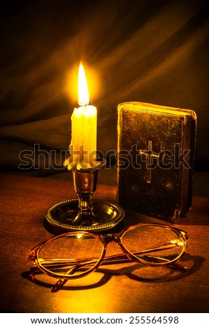 Old bible and candle with glasses on a wooden table. Focus on the candle, image vignetting and in yellow toning