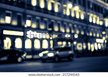 Nights lights of the big city, glowing shop windows and cars on the avenue. Image in yellow-blue toning