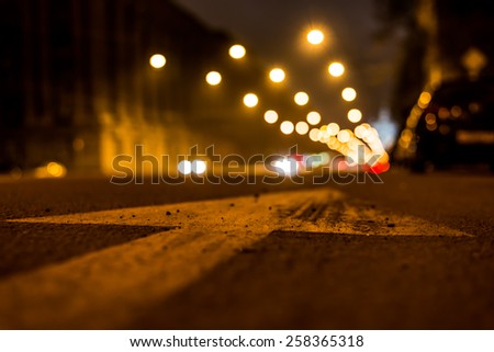 Nights lights of the big city, the night avenue with arrow and headlights of the approaching cars, close up view from asphalt level