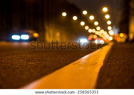 Nights lights of the big city, the night avenue with road markings and headlights of the approaching cars, close up view from asphalt level
