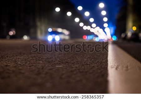 Nights lights of the big city, the night avenue with road markings and headlights of the approaching bus, close up view from asphalt level. In blue tones