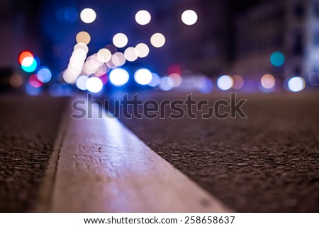 Nights lights of the big city, the night avenue with road markings and headlights of the approaching cars, close up view from asphalt level. In blue tones