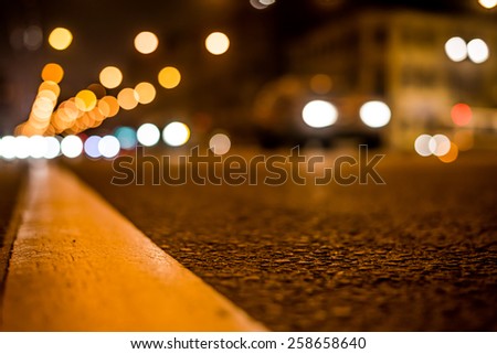 Nights lights of the big city, the night avenue with road markings and headlights of the approaching car, close up view from asphalt level