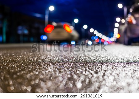 Night city after rain, the car driving on the road. Close up view from asphalt level, in blue tones