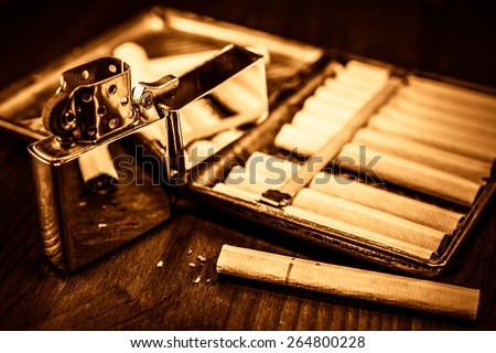 Old cigarette case with cigarettes and lighter on a table in mahogany. Focus on the cigarette, image vignetting and the yellow-orange toning