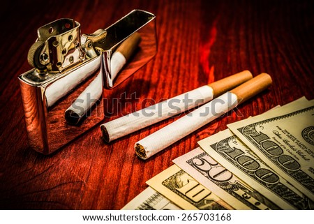 Couple of cigarettes with brown filters and a several dollar bills with lighter on the table. Focus on the cigarettes, image vignetting
