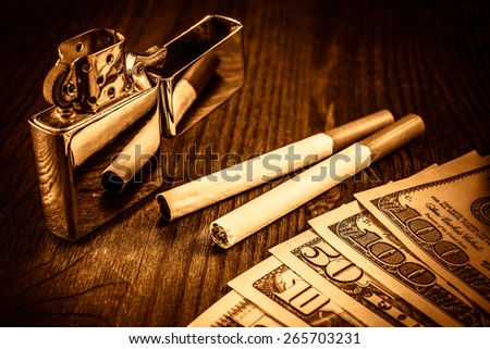 Couple of cigarettes with brown filters and a several dollar bills with lighter on the table. Focus on the cigarettes, image vignetting and the yellow-orange toning